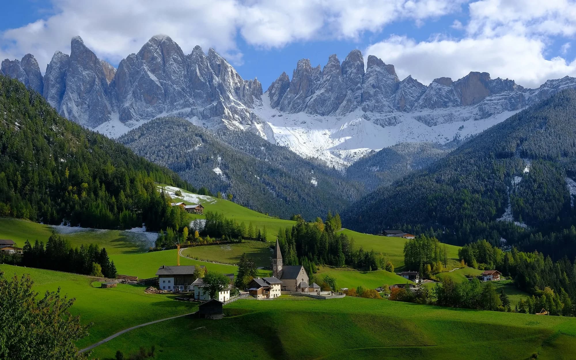 Panorama delle Dolomiti con cime rocciose, prati e case alpine